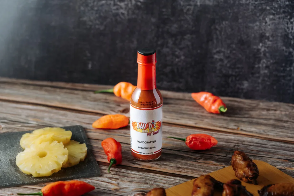 The best hot sauce, David's Been Here Hot Sauce, on a table with peppers, pineapple, and chicken wings | Davidsbeenhere