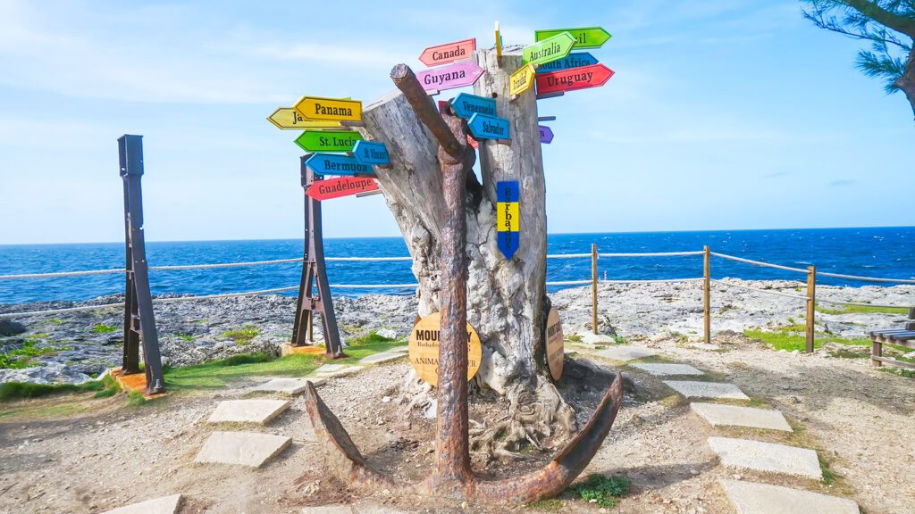 A tree trunk and anchor with colorful signs pointing toward various countries in Barbados | Davidsbeenhere