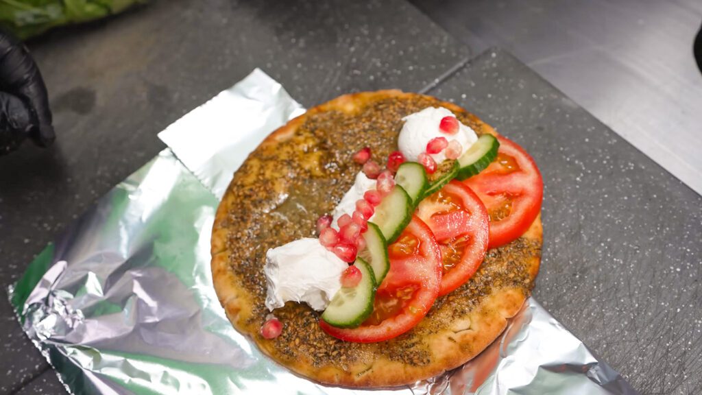 A flatbread sandwich containing za'atar, tomatoes, labneh, cucumbers, and pomegranate seeds | Davidsbeenhere