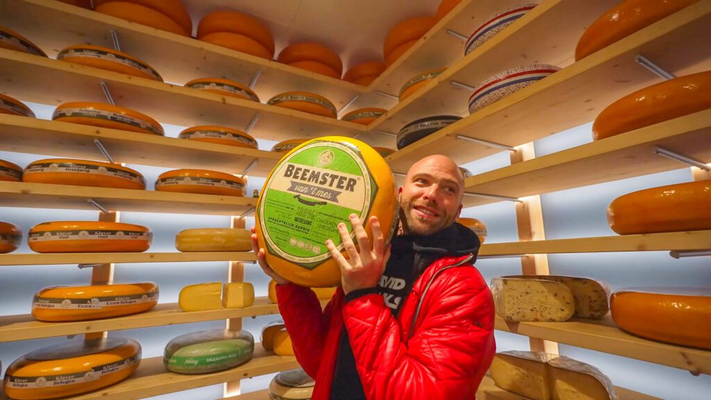 David Hoffmann, surrounded by shelves full of cheese wheels, holding a wheel of cheese | Davidsbeenhere 