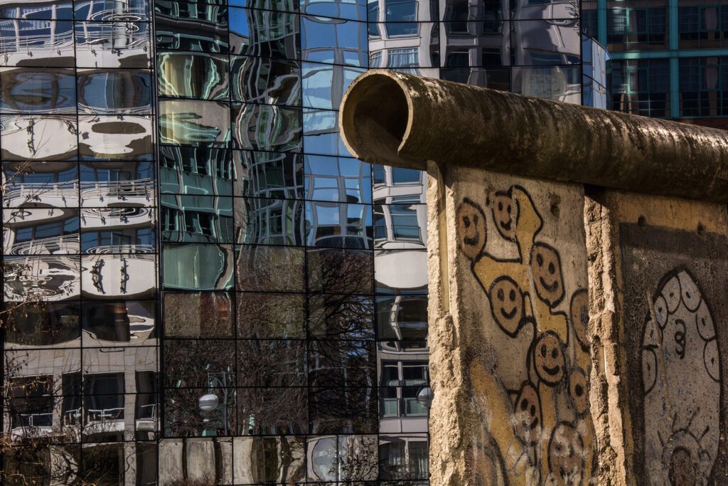 A broken section of the Berlin Wall, one of the top things to do in Berlin, in front of a modern glass building | Davidsbeenhere