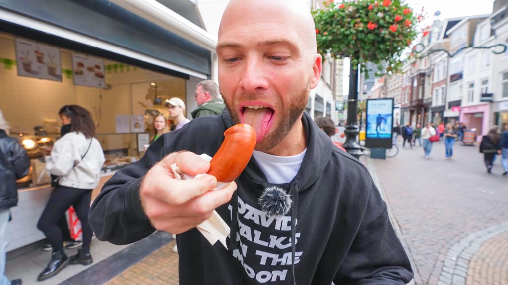 David Hoffmann taking a bite of rookworst, a traditional Dutch sausage, on the streets of Utrecht, the Netherlands | Davidsbeenhere