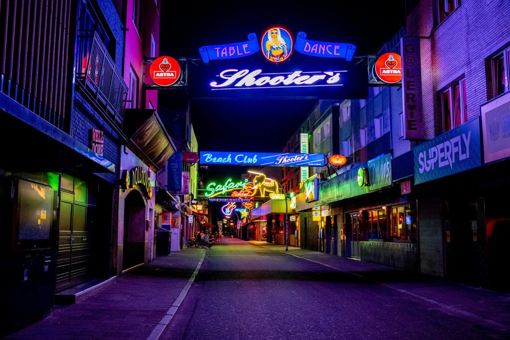 The Reeperbahn at night, with glowing neon signs above various clubs and bars | Davidsbeenhere