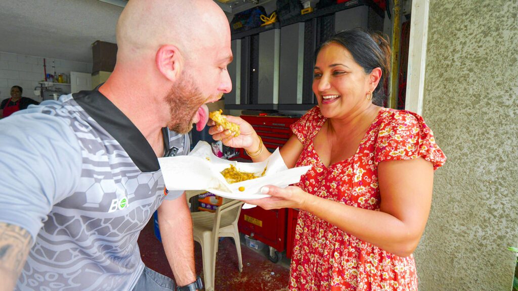 A woman feeds David Hoffmann a bite of her doubles, one of the best Caribbean dishes in the world, at DesiVibes | Davidsbeenhere