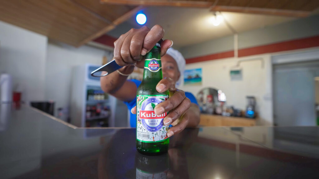 A local woman serves David a bottle of cold, crisp Kabuli lager in Dominica to finish his Dominican food tour | Davidsbeenhere