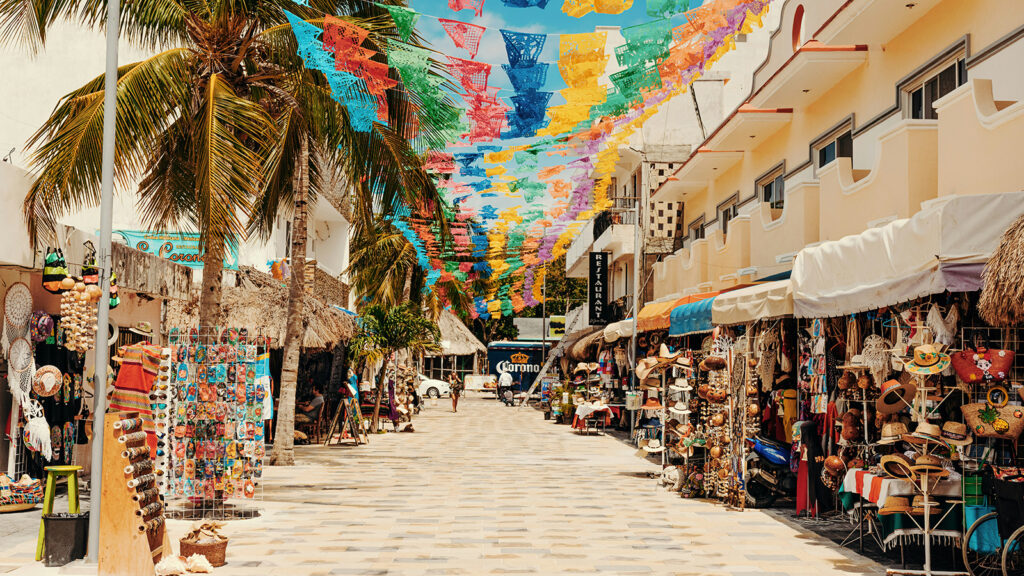 A palm tree lined outdoor market in Cancun, featuring several kiosks and vendors | Davidsbeenhere